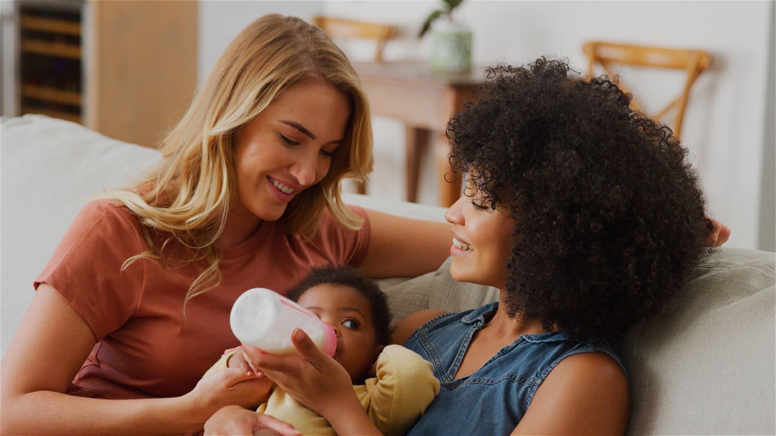 Dos mamás sonriendo mientras su bebé toma la mamadera