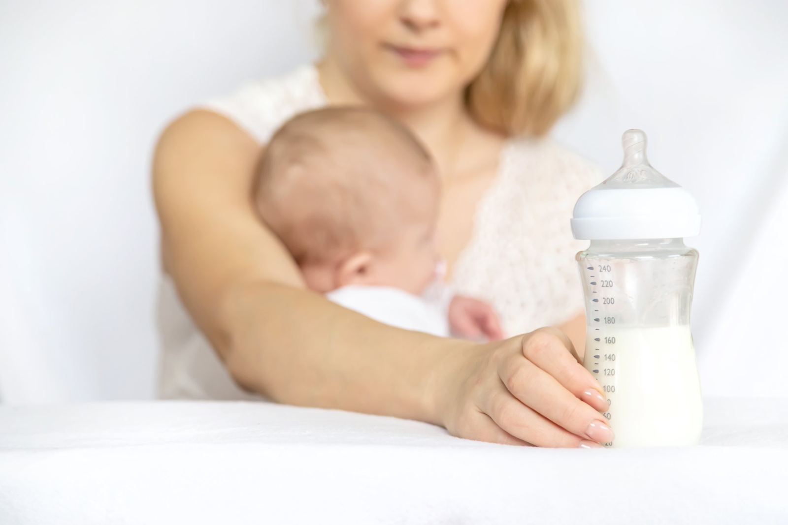 Mamadera con leche junto a una mamá con su bebé en brazos